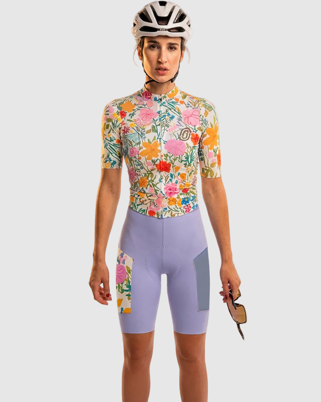 Person wearing a colorful floral cycling jersey and purple shorts with a helmet on a white background